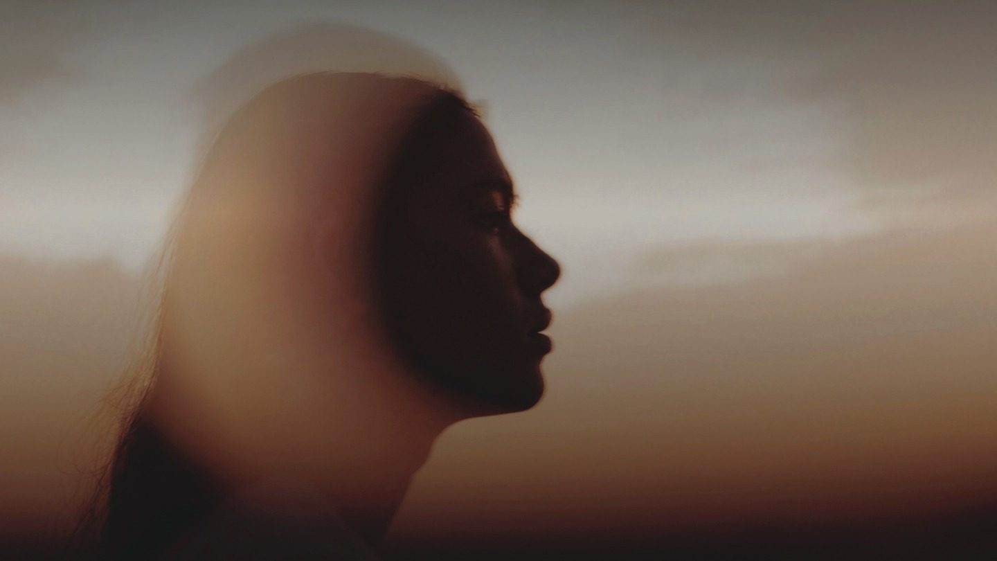 A woman in profile at dusk, a double exposure of her face and the evening sky.