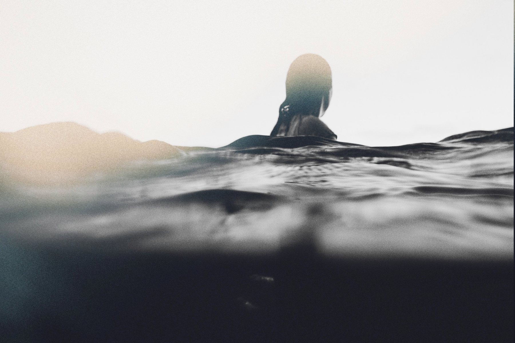 A swimmer in open water at dawn, seen from the surface.